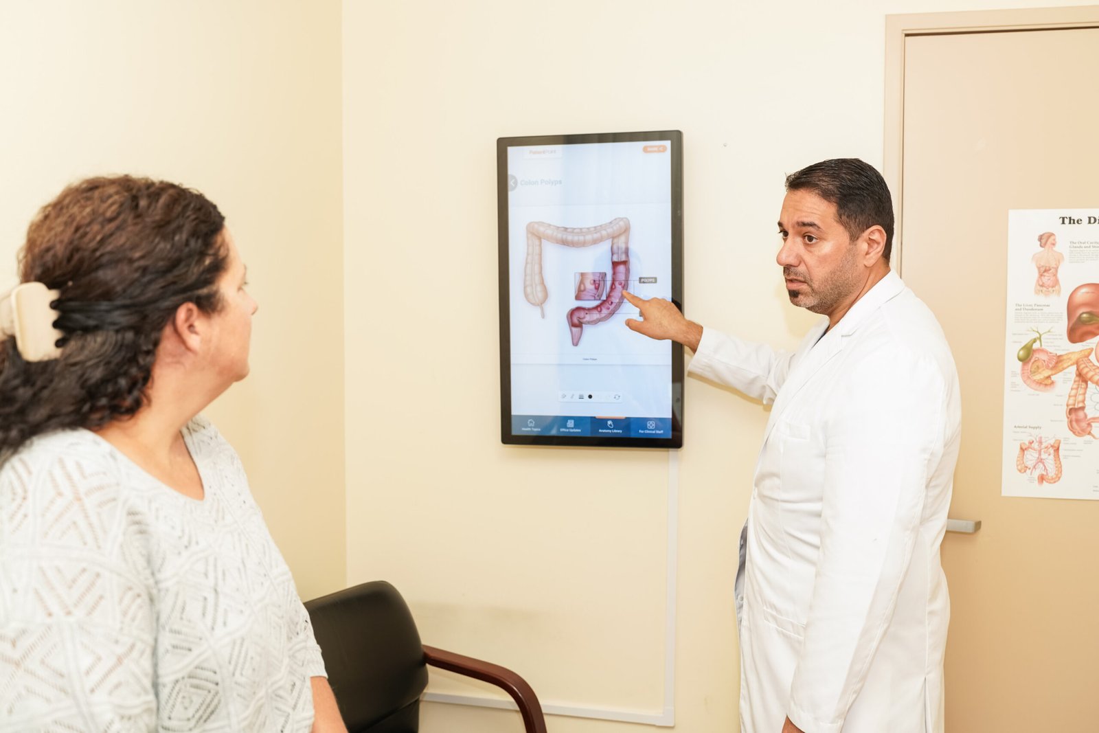 Dr. Mohammed Saadi explaining hemorrhoid treatment on a digital colon diagram to a patient at San Diego Advanced Hemorrhoid Treatment Center.